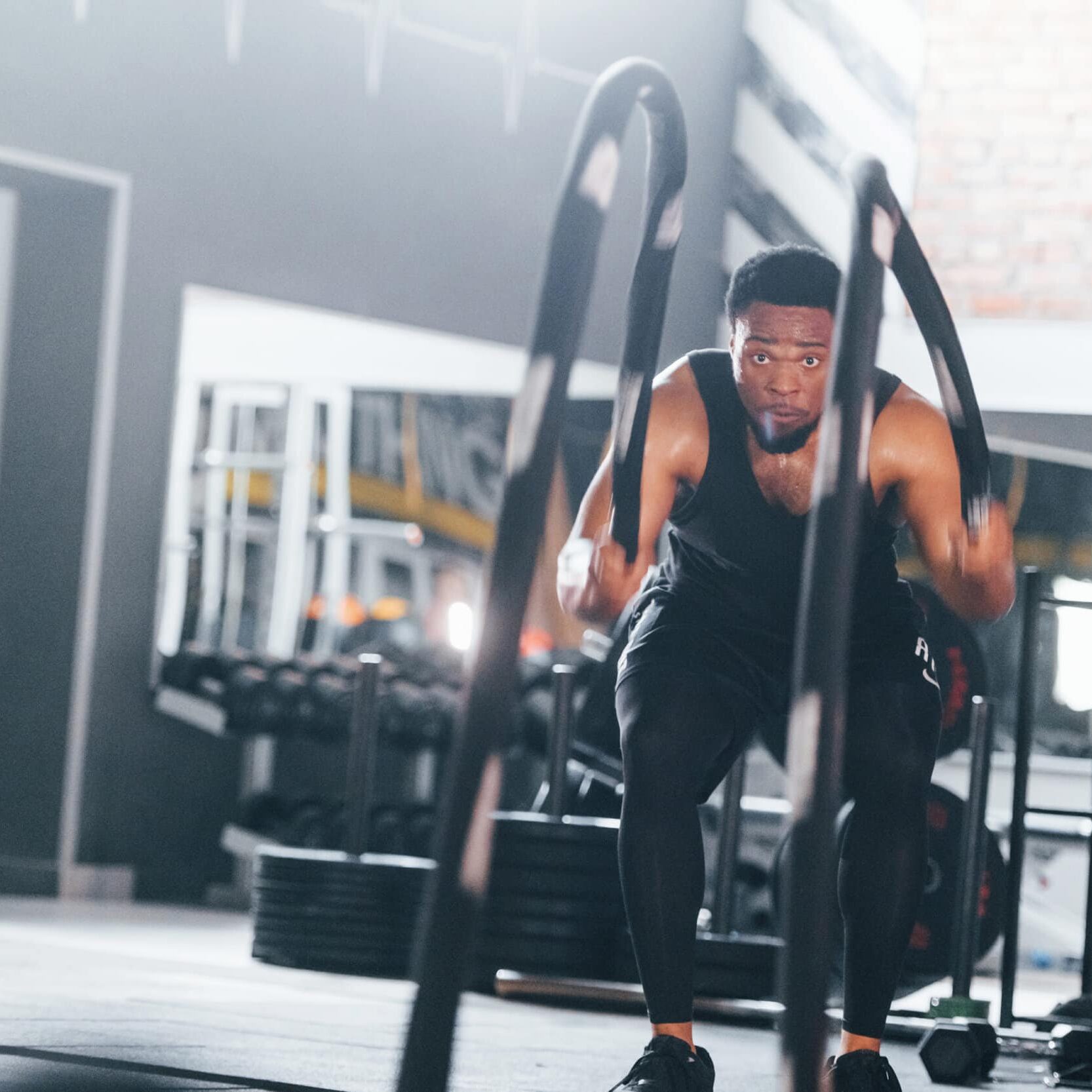 Strong african american man in sportive clothes have workout day in the gym. Doing crossfit by using ropes.